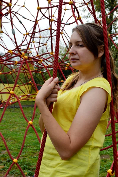 Woman with dark hair in a yellow tank top in a rope park