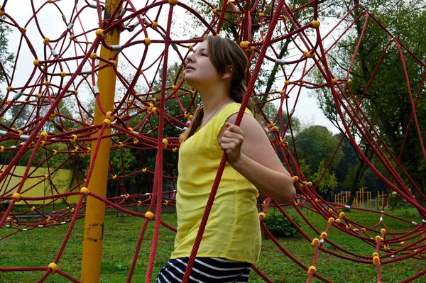 Woman with dark hair in a yellow tank top in a rope park