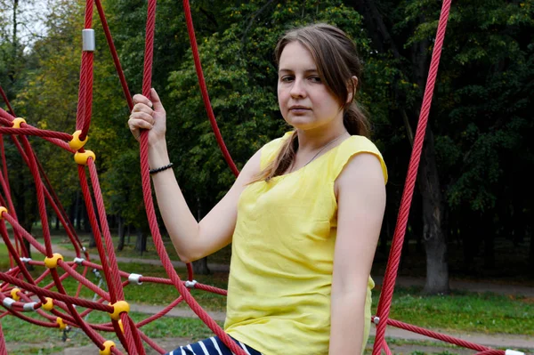 Woman with dark hair in a yellow tank top in a rope park