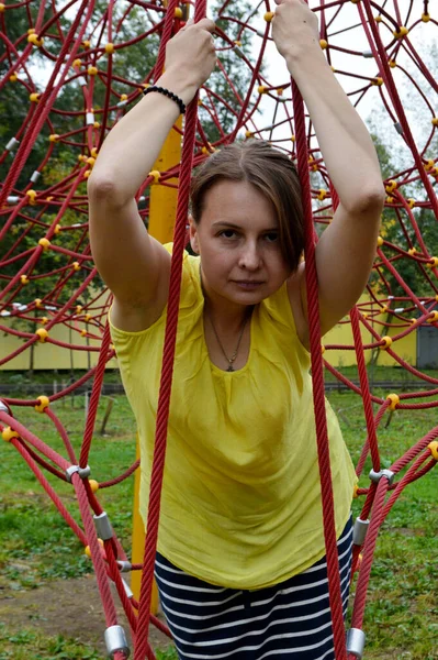 Woman with dark hair in a yellow tank top in a rope park