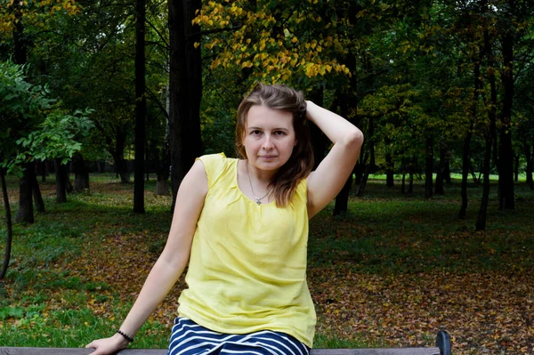 Woman with dark hair in a yellow T-shirt sits on a wooden bench
