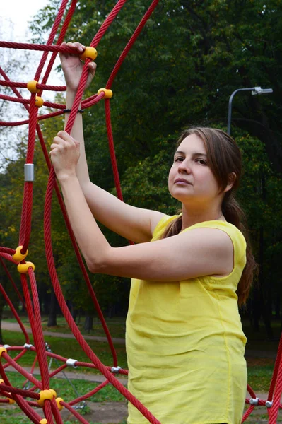 Woman with dark hair in a yellow tank top in a rope park
