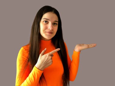 Koyu renk saçlı, parlak turuncu kazaklı, gri arka planda güzel bir kız.