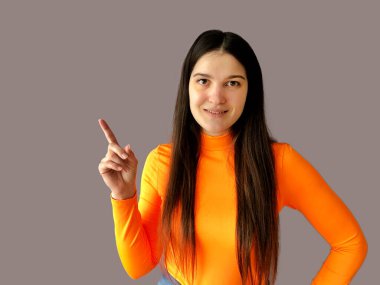 Koyu renk saçlı, parlak turuncu kazaklı, gri arka planda güzel bir kız.