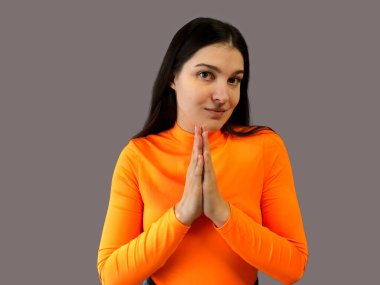 Gri arka planda parlak turuncu süveter giyen koyu renk saçlı güzel bir kız. Yalvarırım.