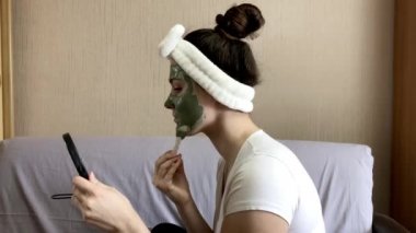 Siyah saçlı, beyaz bandajlı genç ve güzel bir kız elinde bir aynayla oturuyor ve yüzünde jöleli bir maske yapıyor. Evdeki kaplıca.