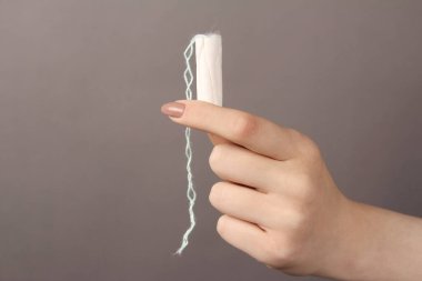 Zarif bir kadın eli, gri arka planda izole edilmiş bir kadın hijyenik bez tutar. Kopyalama alanı