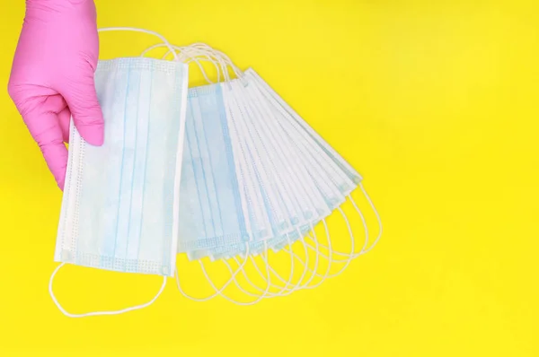 Disposable latex glove. Pink glove. The nurse holds in his hands a blue surgical mask. Security during the quarantine period. Yellow background. Copyspace