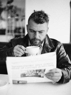 Adam gazete okuyor, kahve içiyor.