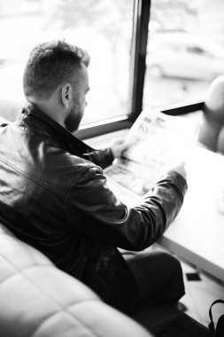 Adam gazete okuyor, kahve içiyor.