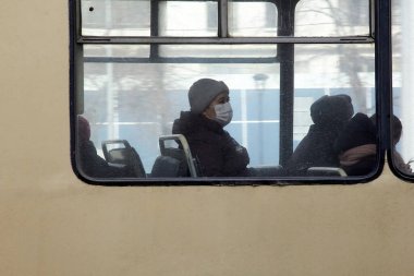 MOSCOW, Rusya - Nisan, 2020. Toplu taşıma araçlarındaki COVID-19 virüsünden yüzünde solunum cihazı olan şapkalı yetişkin bir kadın pencereden dışarı bakıyor. Gündüz, karantina. Halka açık yerlerde insanlara kısıtlamalar.