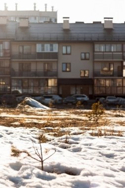 Gündüz vakti park halindeki arabaların olduğu bulanık bir evin arka planında bahar boyunca eriyen kar..
