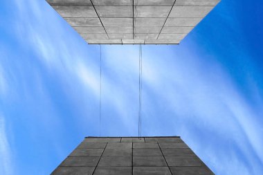 Gri bir evin iki duvarı arasında beyaz bulutlar olan mavi gökyüzünün soyutlanması. Aşağıdan bak. Arkaplan ve doku