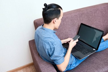 Genç ve güzel bir Asyalı evdeki kanepede dizüstü bilgisayarla çalışıyor. İş adamı sosyal ağlarda çalışır ve iletişim kurar.