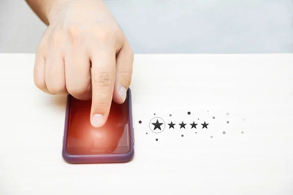 Close-up of a man\'s hand tapping on a smartphone screen with icons of a five-star rating of business service feedback and services. The client gives an excellent rating