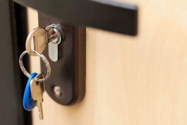 Close-up of metal keys and key chain in the door lock of the house and office. Security concept against hacking of apartments, apartments and offices