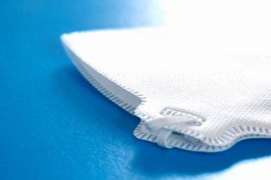 Mavi arka planda yeni koruyucu mavi tıbbi yüz maskesi ve pencereden gelen bir ışık. Viral enfeksiyon salgını sırasında güvenlik ve önleme kavramı COVID-19