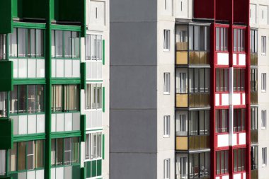 Pencereleri ve renkli duvarları olan balkonları olan yüksek bir apartman. Evlerin somut mimarisi ve ömür boyu apartman inşaatı kavramı