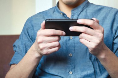 Mavi gömlekli bir işadamı elinde bir cep telefonu tutuyor ve ekranı dinliyor. Çevrimiçi iletişim, iş ve teknoloji kavramı