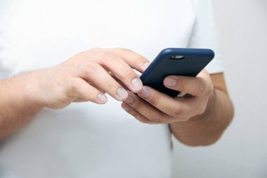 Bir kişi bir telefon tutuyor ve kopyalama alanı olan beyaz bir arkaplanda ekranı dinliyor. Ofiste yaşam tarzı ve mobil internet teknolojileri kavramı