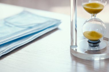 Mavi bir maskenin arka planında kum saati ve virüse karşı korumak için solunum cihazı. Coronavirus COVID-19 salgınının ve hastalığın karantinasının konsepti ve sonu