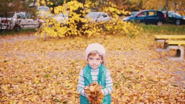 Una niña afuera lanza hojas de otoño al aire y caen en cámara lenta. — Vídeos de Stock