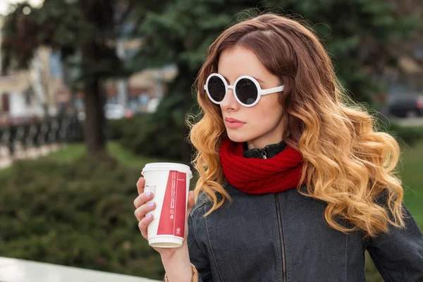 Счастливая молодая женщина в солнечных очках, пьет кофе на открытом воздухе — стоковое фото