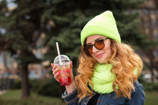 Joyeux jeune femme en lunettes de soleil, chapeau vert clair et écharpe, cocktail en plein air — Photo