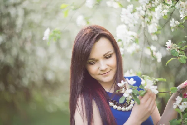 Schöne junge brünette Frau, die an einem warmen Frühlingstag neben dem blühenden Apfelbaum steht — Stockfoto