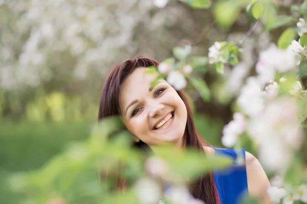 Schöne junge brünette Frau, die an einem warmen Frühlingstag neben dem blühenden Apfelbaum steht — Stockfoto