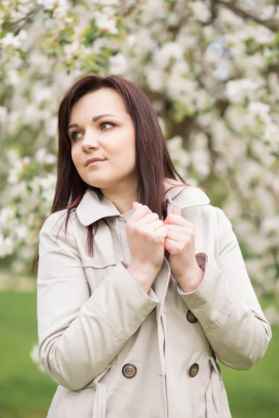 Beautiful young brunette woman standing near the blossoming apple tree on a warm spring day — Stock Photo, Image