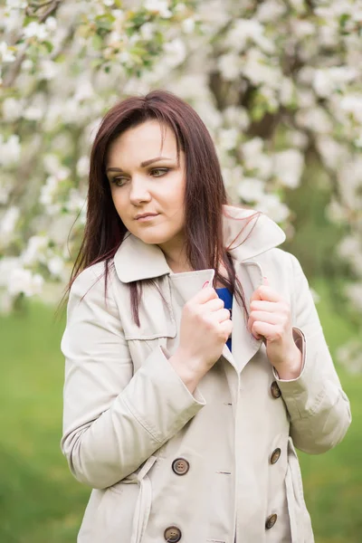 Schöne junge brünette Frau, die an einem warmen Frühlingstag neben dem blühenden Apfelbaum steht — Stockfoto