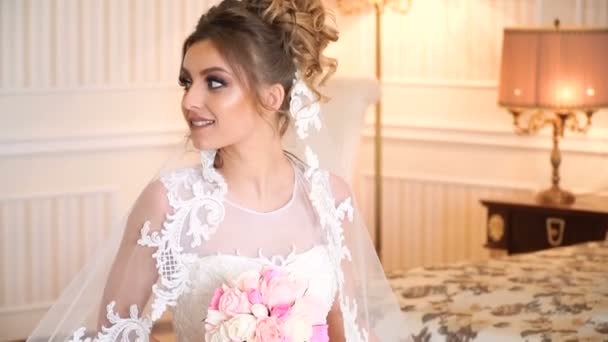 Retrato de la hermosa novia joven. Una chica está posando en una habitación de hotel. Una señora está sentada con un ramo de rosas junto a la ventana. novia esperando en el hotel — Vídeos de Stock