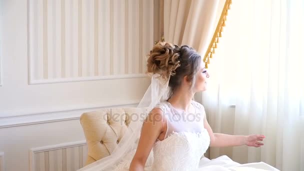 Ritratto di bella giovane sposa. Una ragazza sta posando in una stanza d'albergo. Una signora è seduta con un mazzo di rose vicino alla finestra. sposa in attesa in hotel — Video Stock