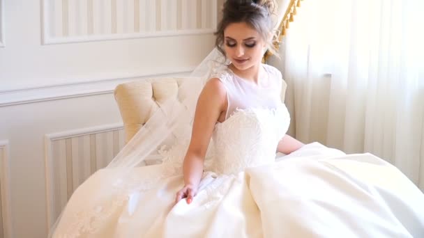 Retrato de la hermosa novia joven. Una chica está posando en una habitación de hotel. Una señora está sentada con un ramo de rosas junto a la ventana. novia esperando en el hotel — Vídeos de Stock