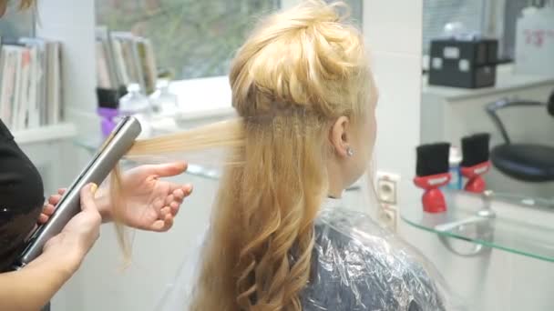 Retrato de una joven en un salón de belleza: creando un magnífico entorno a partir de rizos. Una rubia en una peluquería hace un hermoso peinado. Cuidado del cabello y creación de una imagen . — Vídeos de Stock