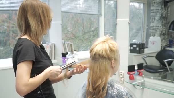 Retrato de una joven en un salón de belleza: creando un magnífico entorno a partir de rizos. Una rubia en una peluquería hace un hermoso peinado. Cuidado del cabello y creación de una imagen . — Vídeos de Stock