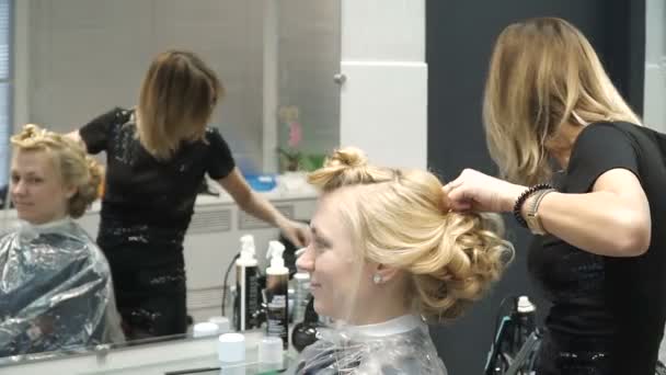 Retrato de una joven en un salón de belleza: creando un magnífico entorno a partir de rizos. Una rubia en una peluquería hace un hermoso peinado. Cuidado del cabello y creación de una imagen . — Vídeo de stock