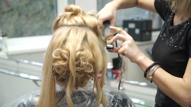 Retrato de una joven en un salón de belleza: creando un magnífico entorno a partir de rizos. Una rubia en una peluquería hace un hermoso peinado. Cuidado del cabello y creación de una imagen . — Vídeos de Stock