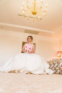 Güzel genç gelin portresi. Bir kız bir otel odasında poz. Bir bayan bir buket gül cam kenarında oturuyor. Otelin bekliyor gelin