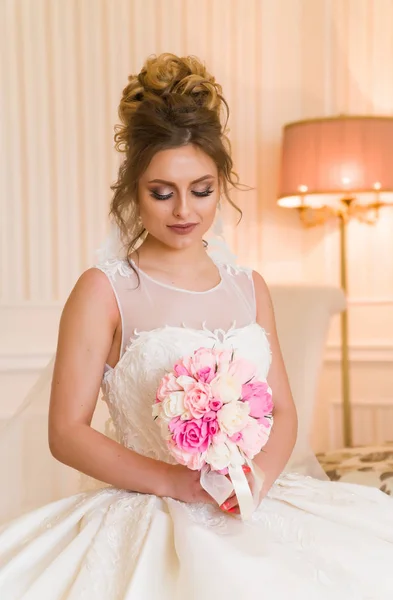 Portret van mooie jonge bruid. Een meisje is poseren in een hotelkamer. Een dame zit met een boeket rozen bij het raam. bruid wachten in hotel — Stockfoto