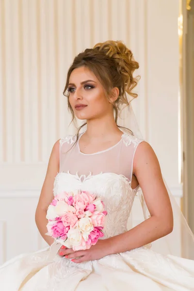 Retrato de la hermosa novia joven. Una chica está posando en una habitación de hotel. Una señora está sentada con un ramo de rosas junto a la ventana. novia esperando en el hotel — Foto de Stock