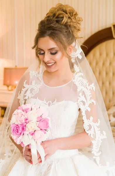 Portret van mooie jonge bruid. Een meisje is poseren in een hotelkamer. Een dame zit met een boeket rozen bij het raam. bruid wachten in hotel — Stockfoto