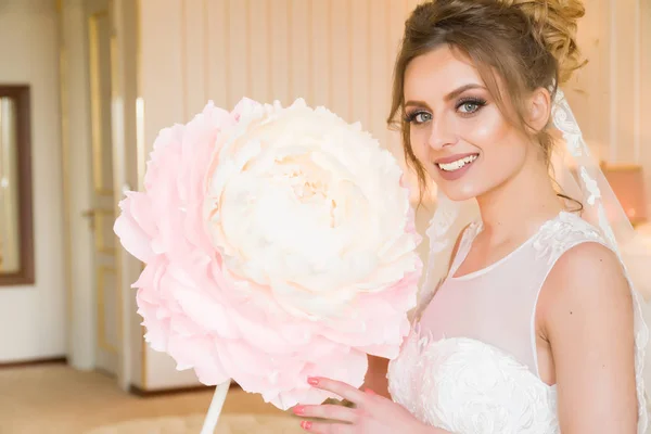 Portrait of beautiful young bride. A girl is posing in a hotel room. A lady is sitting with a paper flower by the window. bride waiting in hotel — Stock Photo, Image