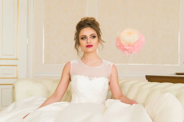 Retrato de bela noiva jovem. Uma rapariga está a posar num quarto de hotel. Uma senhora está sentada com um buquê de rosas junto à janela. noiva esperando no hotel — Fotografia de Stock