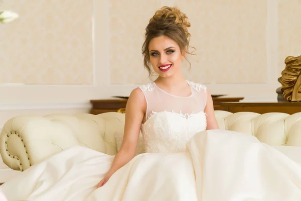 Portret van mooie jonge bruid. Een meisje is poseren in een hotelkamer. Een dame zit met een boeket rozen bij het raam. bruid wachten in hotel — Stockfoto