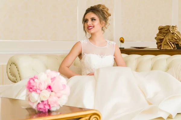 Retrato de bela noiva jovem. Uma rapariga está a posar num quarto de hotel. Uma senhora está sentada com um buquê de rosas junto à janela. noiva esperando no hotel — Fotografia de Stock