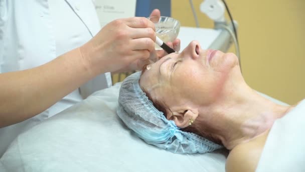 Preparazione di una donna anziana per la procedura di sollevamento RF in una clinica di cosmetologia. Applicare il gel sul viso . — Video Stock