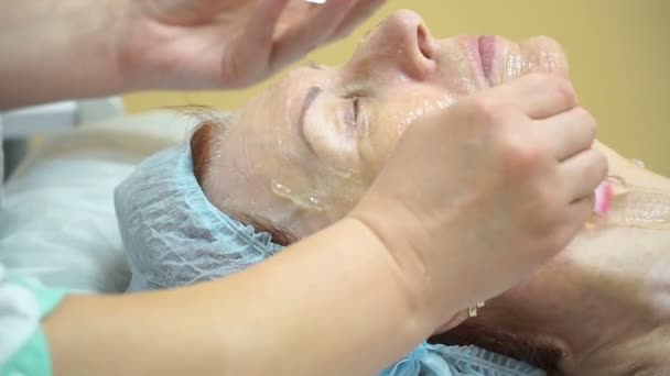 Voorbereiding van een oudere vrouw voor Rf procedure tillen in een kliniek cosmetologie. Toepassing van gel gezicht. — Stockvideo