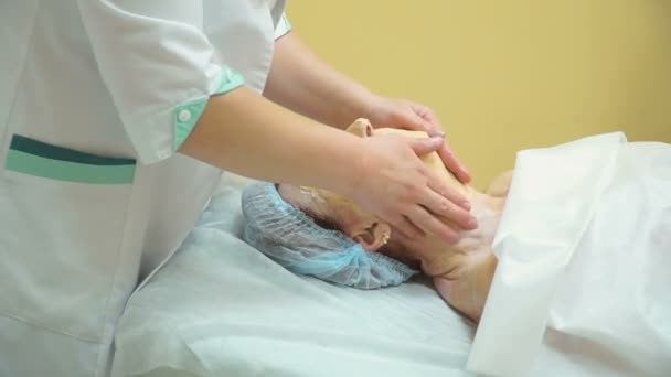 Uma mulher idosa recebe uma massagem facial profissional após o levantamento do procedimento de RF em uma clínica de cosmetologia . — Vídeo de Stock